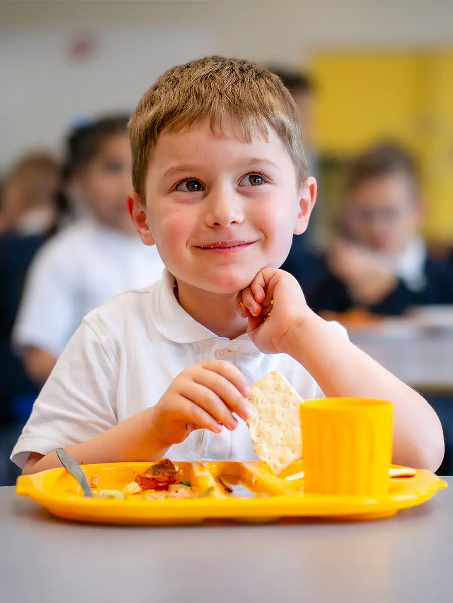 Young boy eating lunch at table smiling upwards